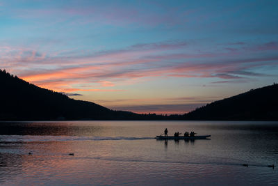 Silhouette people on lake against sky during sunset