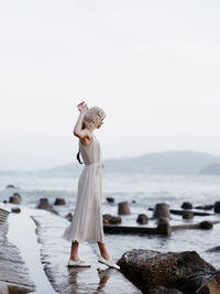 Rear view of woman standing at beach against sky