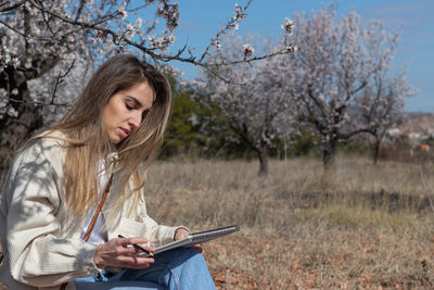 Young woman using mobile phone while sitting on field