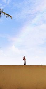 Low angle view of hand on wall against sky