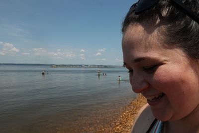 Close-up of smiling young woman at beach against sky