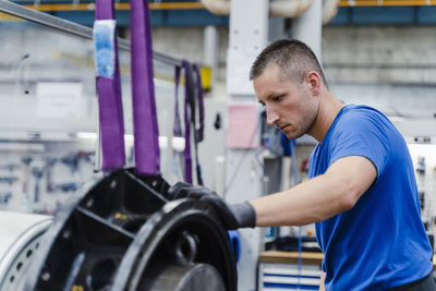 Male manual worker concentrating while doing quality check of machinery at illuminated factory