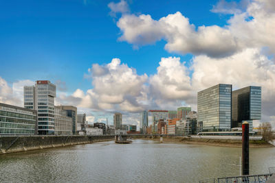 Buildings by river against cloudy sky