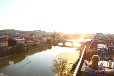 Rear view of man by river against buildings in city