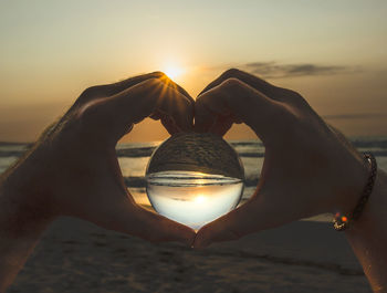 Cropped hand of woman holding crystal ball against sky