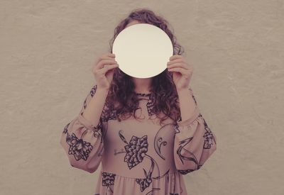 Woman holding umbrella standing against wall