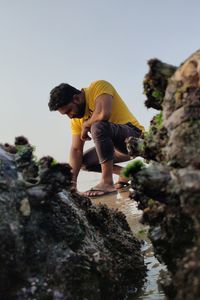 Full length of young man standing on rock against sky