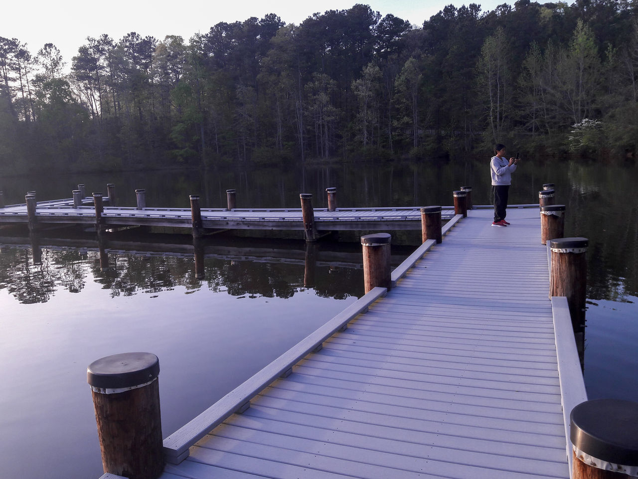 MAN STANDING ON PIER AMIDST LAKE