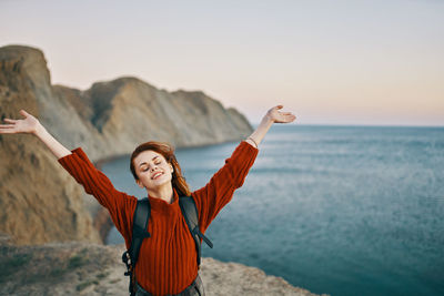 Man with arms raised standing in sea against sky