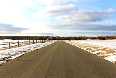 Road amidst snow covered landscape against sky