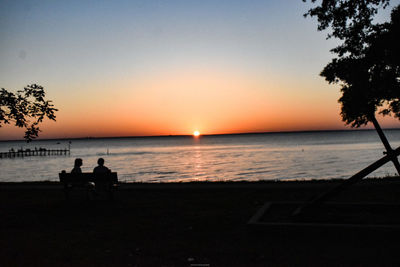 Silhouette people sitting on beach against sky during sunset