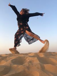 Low angle view of woman jumping on sand at desert against sky