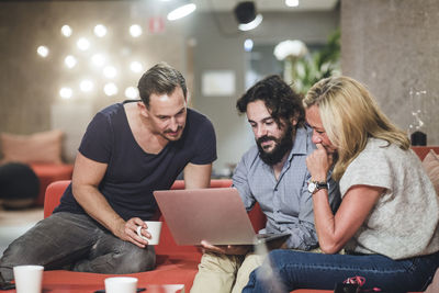 Young businessman using laptop while sitting with coworkers in office