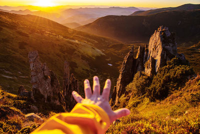 Person hand on mountain against sky during sunset