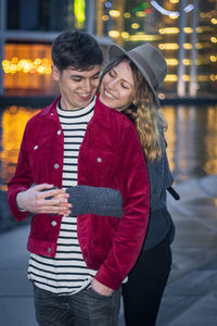 Cheerful girlfriend embracing boyfriend on promenade in city