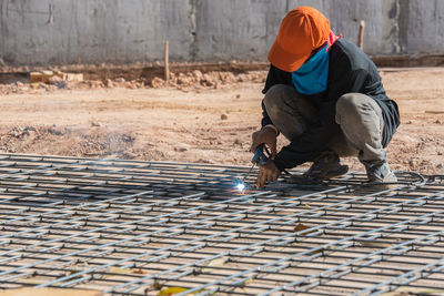 Full length of worker couching on metal grate while welding