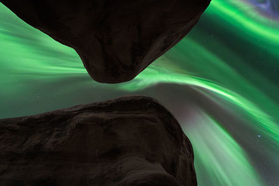 Through hole in rocky mountains view of dark night sky with glowing green polar lights in norway