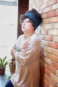 Woman looking away while standing against brick wall