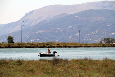 Man boating on lake against mountain during foggy weather