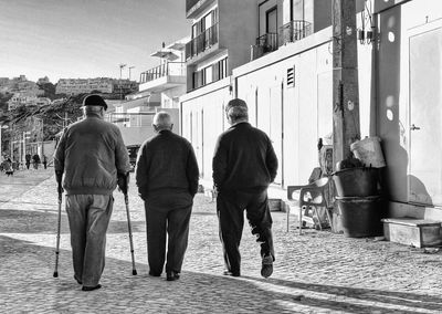 Full length rear view of senior people walking on footpath by house against sky