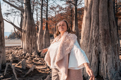 Woman standing by tree trunk in forest