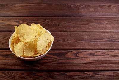 Cheese and chive potato crisp snack in brown bowl on wooden background