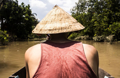 Rear view of man wearing hat sitting in boat on lake