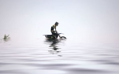 Man riding dirt bike in lake against sky