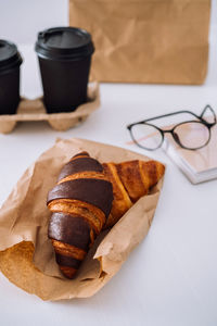 Delicious chocolate and brown croissants and coffee cups at workplace with glasses and notebook