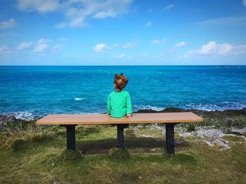 Rear view of girl sitting on seat by sea against sky