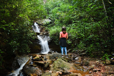 Woman standing on rock against waterfall in forest