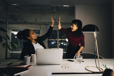 Cheerful female entrepreneurs giving high-five while working late in office