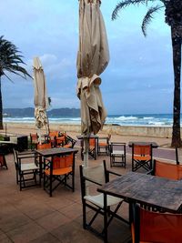 Chairs and tables at beach against sky