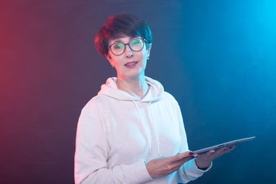 Portrait of young woman standing against black background