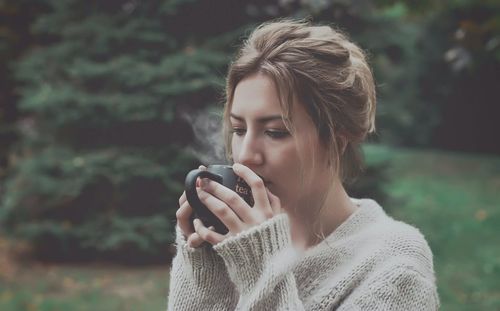 Close-up of woman drinking coffee against tree