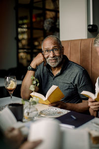 Senior man wearing eyeglasses sitting with book in cafe