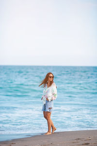 Young woman standing at beach against clear sky