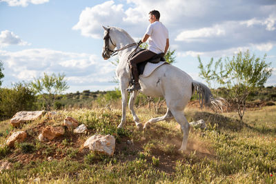 Side view of man riding horse on land against sky