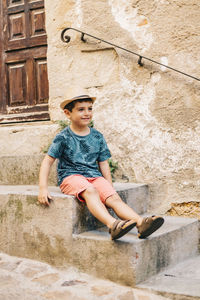 Full length of cute boy wearing hat sitting on steps