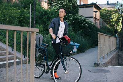 Mid adult man walking with bicycle on footpath in city