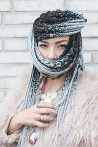 Beautiful woman with braided hair standing against wall