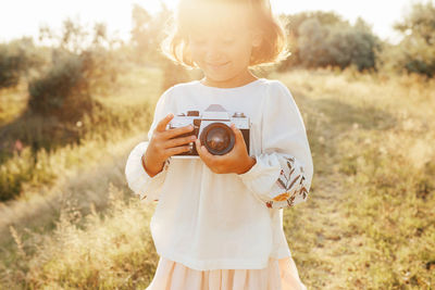 Midsection of child holding camera while standing on field