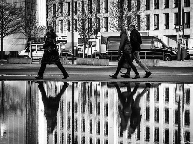 building exterior, lifestyles, full length, architecture, built structure, city, leisure activity, casual clothing, young adult, standing, city life, walking, street, men, day, reflection, building, person