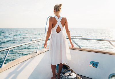 Rear view of woman standing in boat on sea against sky