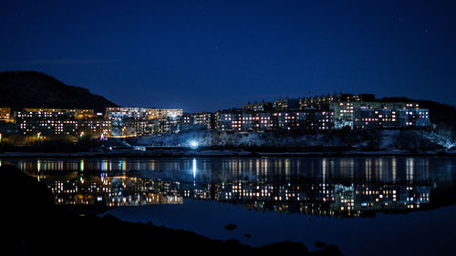 Illuminated cityscape against clear blue sky at night