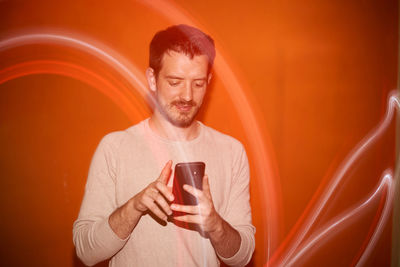 Young man looking the smartphone on a orange colored background