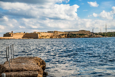 Buildings by sea against cloudy sky