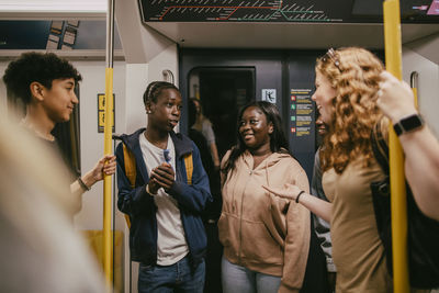 Multiracial male and female friends talking with each other while travelling through subway train