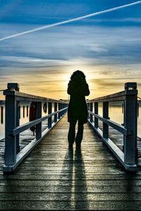 Silhouette man standing on footbridge against sky during sunset