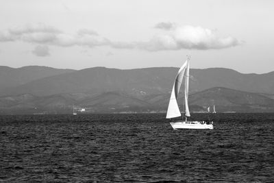 Sailboat sailing on sea against mountains